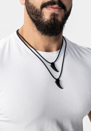 Black beaded necklaces with two pointed pendant charms in a claw shape, hanging on a simple braided cord, worn over a white shirt.