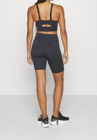 Soutien-gorge de sport noir avec bretelles ajustables et détail découpé au dos, associé à un short de vélo noir près du corps et des chaussures de sport noires.