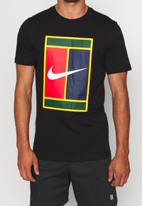 Camiseta negra con un gran diseño de logotipo rectangular multicolor. El logotipo tiene secciones en rojo, azul marino y verde con un swoosh blanco de Nike.