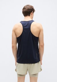 Μπλε σκούρο αθλητικό τοπ χωρίς μανίκια με σχεδιασμό racerback, κατασκευασμένο από υλικό που απομακρύνει την υγρασία, σε συνδυασμό με ανοιχτό μπεζ σορτς.