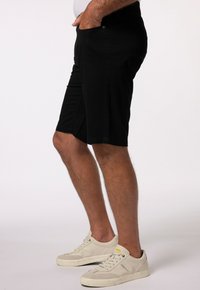 Pantaloni corti neri in misto cotone, con taglio dritto, tasche laterali e dettagli di cucitura sottili, abbinati a sneakers beige chiaro.