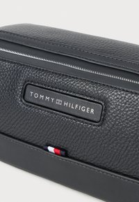 Tommy Hilfiger sort læder lynlåsetui med tekstureret overflade, der har en logo-plade og en lille rød, hvid og blå stribe detalje.