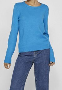 Pull en maille bleu à manches longues, col rond, poignets et ourlet côtelés ; associé à un pantalon en denim bleu. Texture douce, coupe décontractée.