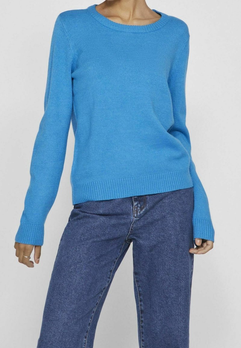 Pull en maille bleu à manches longues, col rond, poignets et ourlet côtelés ; associé à un pantalon en denim bleu. Texture douce, coupe décontractée.