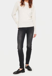 Kremowy sweter z bufiastymi rękawami, zestawiony z czarnymi spodniami slim fit i czarnymi loafersami. Gładka faktura, minimalne detale i elegancki design.