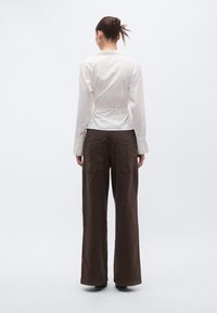 Λευκό πουκάμισο με μακριά μανίκια, εφαρμοστό στη μέση και ανοιχτό γιακά, σε συνδυασμό με φαρδιά καφέ παντελόνια με δύο πίσω τσέπες.