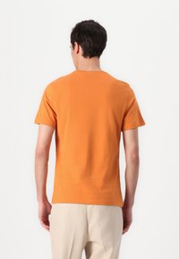 T-shirt de algodão laranja com mangas curtas e decote redondo, textura suave e design simples. Detalhe de costura visível na bainha.