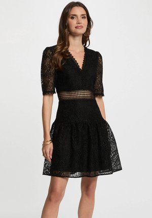 Black lace dress with a deep V-neck, short puff sleeves, and a fitted waist. Features a textured pattern and a flared skirt.