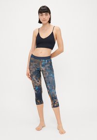 Kék, barna és fekete verőfényes mintájú capri leggings, testhez simuló kialakítással. A szettet egy illeszkedő sötét sportmelltartó egészíti ki.