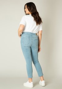 Lichtblauwe high-waisted jeans met rafelige enkelranden en twee achterzakken, gecombineerd met een witte T-shirt met korte mouwen en witte sneakers.