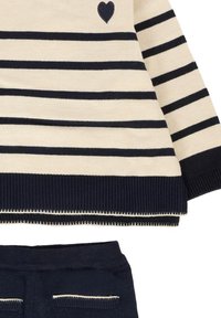 Maglione a righe in crema e blu navy, con un piccolo dettaglio a forma di cuore e polsini a coste testurizzati; pantaloni blu navy abbinati con rifiniture a contrasto.