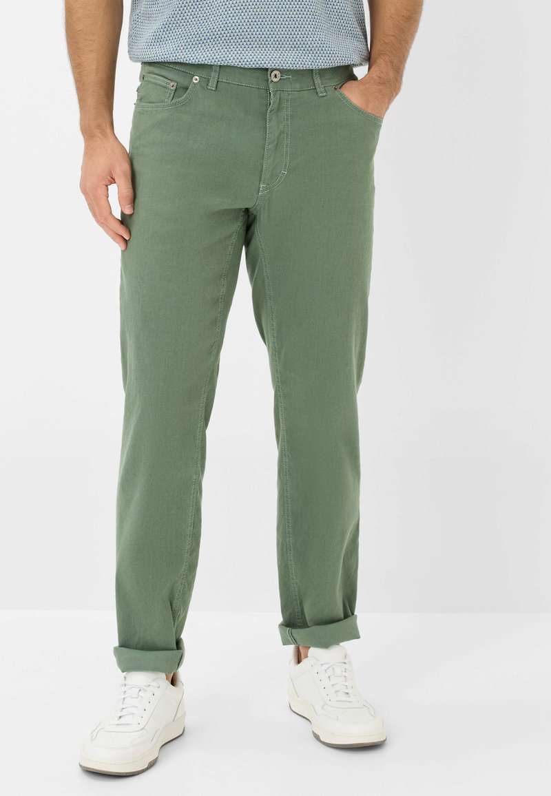 Pantalons en mélange de coton vert avec une coupe droite, dotés de revers, de poches avant et d'une fermeture à bouton. Portés avec des baskets blanches.
