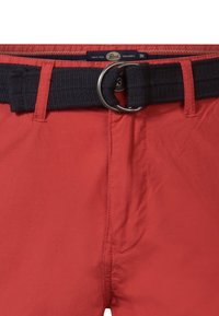 Pantaloni scurți roșii cu un brâu țesut bleumarin, dotat cu o cataramă în formă de D din argint. Materialul are o textură netedă și detalii de cusătură minimale.