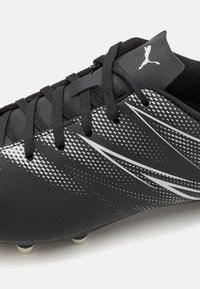 Botín de fútbol negro con patrones de acento blancos, superficie texturizada y cordones. Presenta seis tacos blancos en la suela para mayor tracción.