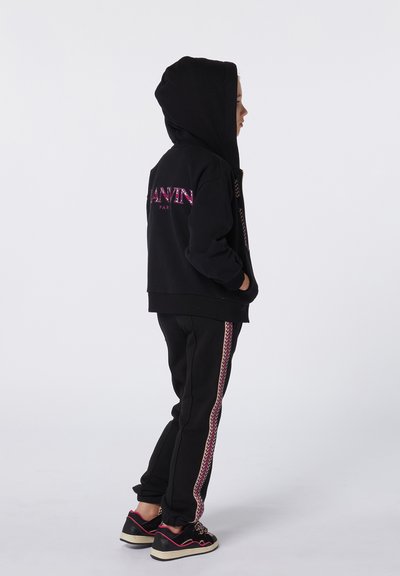 Sweat à capuche noir avec logo rose et pantalon noir assorti présentant une bande en chevron rose. Stylé avec des baskets noires.