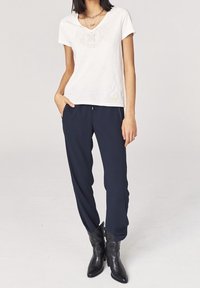 Camiseta blanca de manga corta con cuello redondo y un gráfico frontal, combinada con pantalones navy ajustados y botas negras hasta el tobillo.