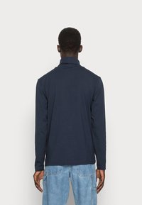 Mörkblå långärmad skjorta med krage, slät textur och rak passform. Bärs tillsammans med ljusblå cargo-byxor som visar fickor och sömdetaljer.