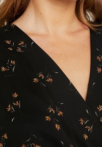 Schwarzes Kleid mit tiefem V-Ausschnitt, das mit einem floralem Muster in Orange und Grün gestaltet ist. Der Stoff ist glatt mit einer dezenten Textur.