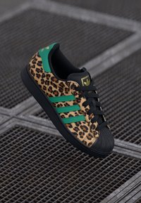 Sneaker con stampa leopardata, punta nera, dettagli verdi e tre strisce verdi. Lacci neri e suola in gomma testurizzata completano il design.