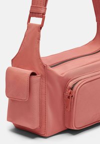 Różowa torebka na ramię wykonana z teksturowanej tkaniny, z zasuwaną główną przegrodą, boczną kieszenią oraz regulowanym paskiem z metalowymi akcentami.