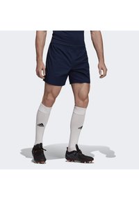 Marineblaue Sportshorts mit elastischem Bund, kombiniert mit weißen knielangen Socken mit schwarzem Logo und schwarzen Fußballschuhen mit orangefarbenen Akzenten.