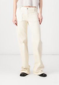 Jeans de pierna ancha color crema, confeccionados en denim, con dos bolsillos frontales y cierre de botón. La tela tiene una textura suave.
