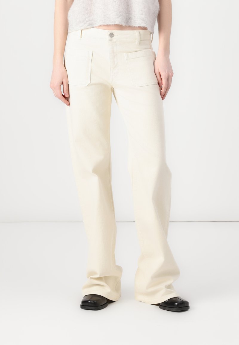 Jeans de pierna ancha color crema, confeccionados en denim, con dos bolsillos frontales y cierre de botón. La tela tiene una textura suave.