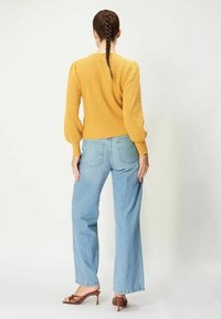 Gul texturerad stickad tröja med långa puffärmar, matchad med ljusblå högmidjade raka jeans och bruna klacksandaler.
