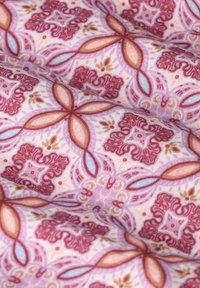 Gemusterter Stoff mit floralem Design in Rot, Pink und Blau auf einem hellrosafarbenen Hintergrund. Glatte Textur mit feinen Details.