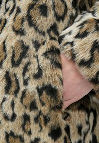 Pele falsa com padrão de estampa de leopardo em tons de castanho claro e preto; apresenta textura macia e um bolso lateral oculto para a mão.