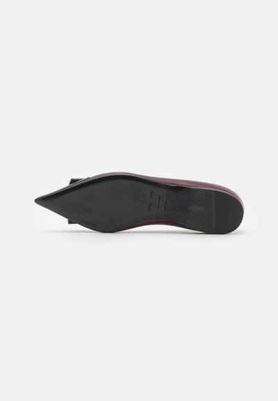 Zapato de punta afilada con un upper color burdeos, suela negra y textura suave. Presenta un tacón plano y un diseño minimalista.