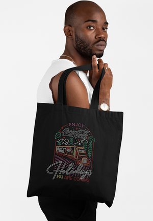 Borsa a tracolla nera con una vivace grafica natalizia della Coca-Cola, un camion e alberi di pino, con dettagli di testo bianchi e colorati a contrasto.