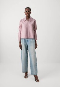 Fleecejacka med dragkedja i ljusrosa, avslappnad passform, kombinerad med ljusblå vida jeans och svarta högklackade sandaler. Mjuk textur.