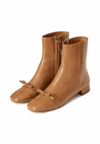 Botas de tobillo de cuero marrón con punta cuadrada, cierre de cremallera y un detalle decorativo de lazo en la parte delantera. Tacón plano, textura suave.