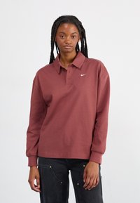 Bordový polo svetr s dlouhým rukávem vyrobený z bavlny, s klasickým límečkem, tříknoflíkovou légou a malým bílým logem Nike na hrudi.