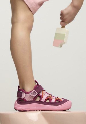 Sandalias infantiles moradas y rosas con parte superior de malla, correas ajustables y suela de goma. La sandalia presenta cordones coloridos y un diseño con cortes.