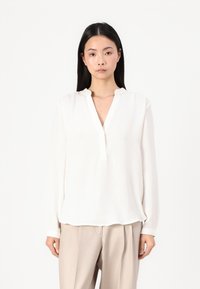 Hvit langermet bluse med mandarinkrage, med en avslappet passform og myk tekstur, kombinert med beige bukser.