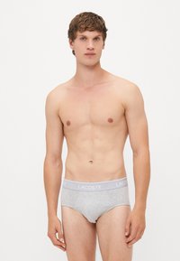 Graue Unterwäsche im Brief-Stil mit weichem Material, ausgestattet mit einem hellgrauen Bund, auf dem "LACOSTE" steht. Einfaches Design, körpernahe Passform.