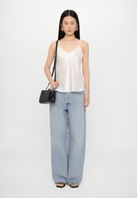 Camisole en satin blanc avec des bretelles fines, associée à un jean large bleu clair. Sac à bandoulière noir et sandales à talons noires.