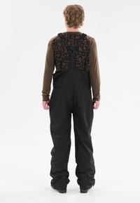 Mustat hiihtobibit säädettävillä olkaimilla, tekstiilipinta, suuret taskut ja kuvioitu takakappale, jossa on sana "SLOPE" ruskealla.