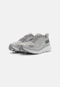 Scarpe da corsa grigie con tomaia in mesh, motivo testurizzato e suola arrotondata. Presentano un branding discreto e un sistema di chiusura con lacci per una vestibilità sicura.