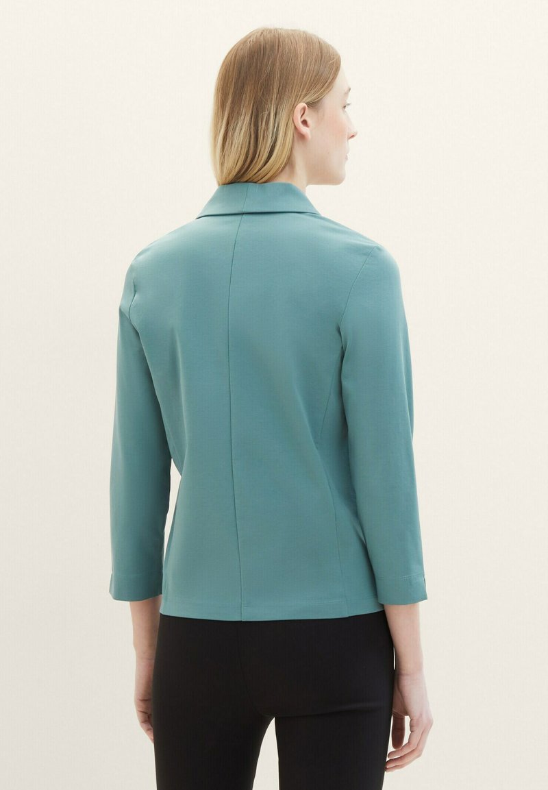 Teal-coloured blazer met driekwartmouwen, soepele textuur, gestructureerde kraag en achterste seam details, gecombineerd met zwarte broek.