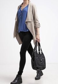 Beige lightweight jacket over a blue blouse with buttons, black leggings, and ankle boots. Carrying a black leather handbag with zipper.