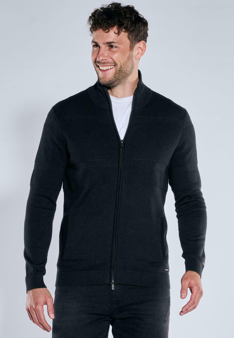 Reißverschluss-Strickjacke aus dunkelblauem Strickmaterial mit strukturiertem Muster, gerippten Bündchen und Saum. Verfügt über einen Stehkragen und seitliche Taschen.