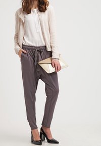 Beige gebreide cardigan, witte blouse, slate grijze harem broek, zwarte lakleren hakken, met een crèmekleurige clutch, zachte texturen en ontspannen pasvorm.