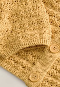 Tissu tricoté jaune avec un motif en losange texturé et deux grands boutons jaunes assortis sur le bord.