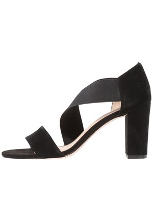 Czarne zamszowe sandały na wysokim obcasie z szerokim elastycznym paskiem wzdłuż łuku stopy oraz wyściełaną wkładką. Posiadają masywny blokowy obcas.