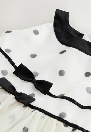 Fehér ruha fekete pöttyökkel, fekete selyem gallérral és két fekete masnival. Áttetsző anyag és pliszírozott szegély.