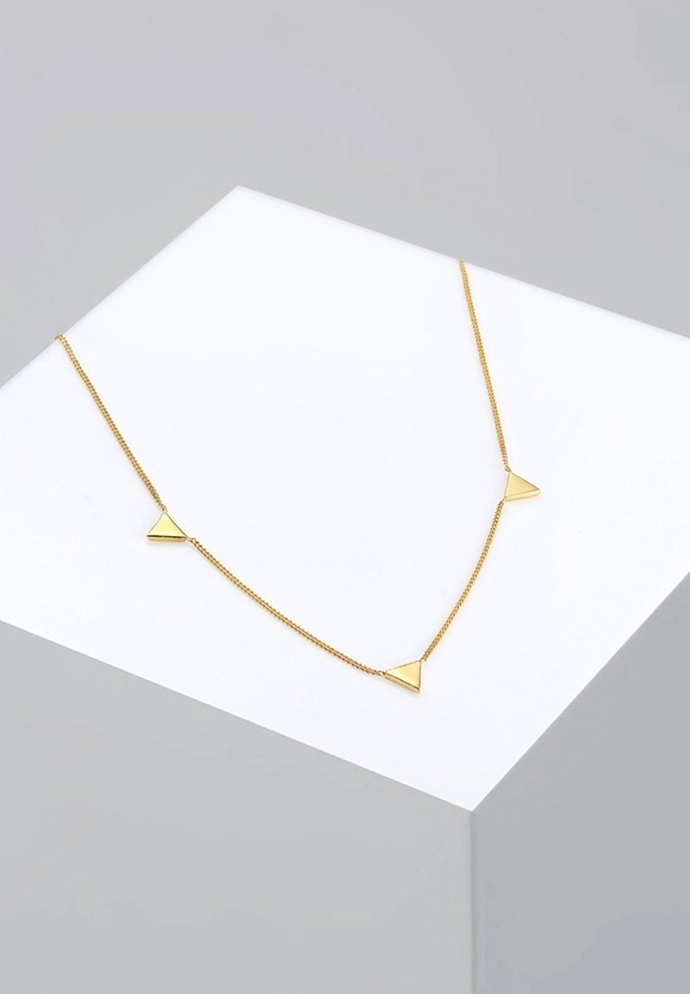 Collier délicat en chaîne d'or avec trois petits pendentifs triangulaires espacés régulièrement, présenté sur une surface blanche inclinée.