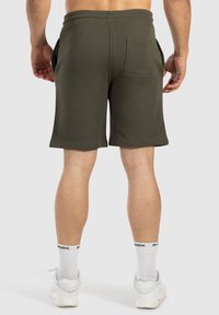Pantalones cortos de algodón de color verde oscuro con dos bolsillos laterales y un bolsillo trasero. Cuenta con una cinturilla plana y una textura acanalada.